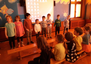 Dzieci z grupy VI stoją przy tablicy multimedialnej i śpiewają piosenkę Europo nasza dla dzieci z grupy V.